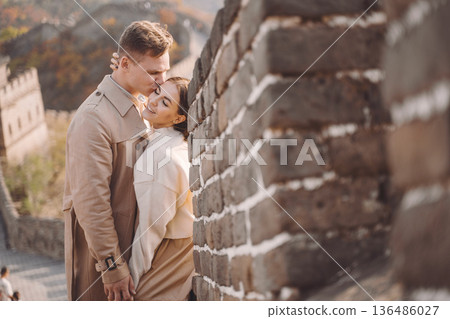 beautiful young couple hugging at the Great Wall of China. Newly married couple on their honemoon to Great Wall near Beijing China. Stylish couple exploring one of the wonders of the world. beautiful young couple hugging at the Great Wall of China. Newly married couple on their honemoon to Great Wall near Beijing China. Stylish couple exploring one of the wonders of the world. 136486027