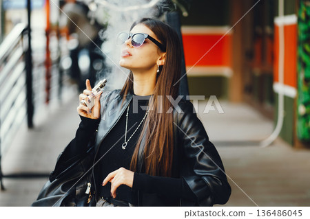 stylish girl smoking an e-cigarette as she is walking through the city stylish girl smoking an e-cigarette as she is walking through the city 136486045