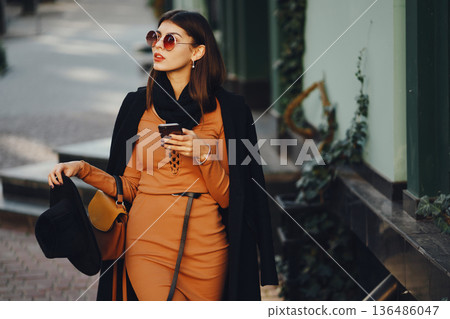 styligh woman uses her cell phone as she walks through the city on a sunny warm day styligh woman uses her cell phone as she walks through the city on a sunny warm day 136486047