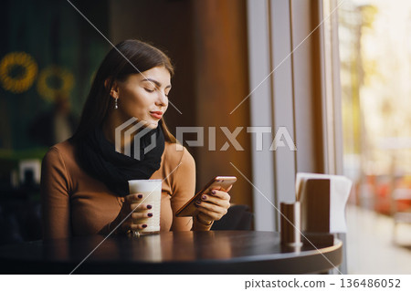 brunette girl using her phone while drinking coffee at a restaurant brunette girl using her phone while drinking coffee at a restaurant 136486052