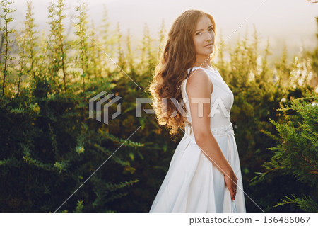 Beautiful long-haired bride in a magnificent white dress walking in nature Beautiful long-haired bride in a magnificent white dress walking in nature 136486067
