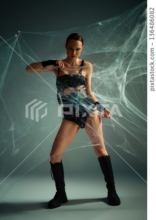 Powerful woman in black gothic costume tangled in a studio spiderweb Powerful woman in black gothic costume tangled in a studio spiderweb 136486082