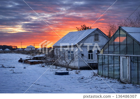 Cold Winter Countryside with Snowy Houses Under Dramatic Evening Sky Cold Winter Countryside with Snowy Houses Under Dramatic Evening Sky 136486307