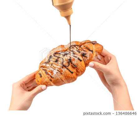 Chocolate syrup pouring over caramel croissant in female hands isolated on white 136486646