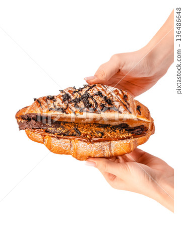 Stuffed chocolate and caramel croissant with nuts held in female hands isolated on white 136486648