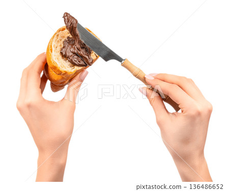 Spreading chocolate cream on croissant with knife in female hands isolated on white Spreading chocolate cream on croissant with knife in female hands isolated on white 136486652
