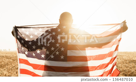 Person holding American flag in sunlight with wheat field in background during golden hour Person holding American flag in sunlight with wheat field in background during golden hour 136487010
