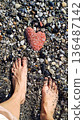 Finding a heart-shaped stone on a beach during a sunny day while standing barefoot in warm sand and cool water 136487142