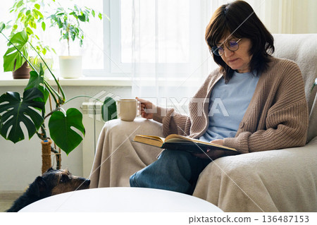 Woman relaxing at home with dog and book 136487153