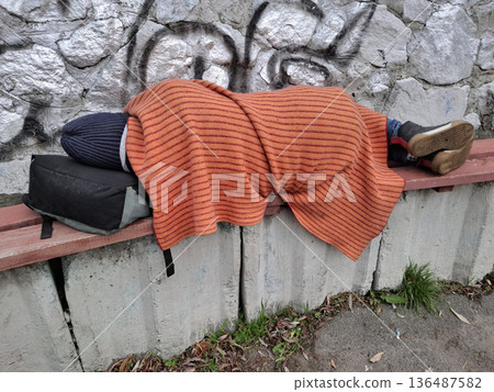 Homeless destitute man in hat and red cover sleep on bench 136487582