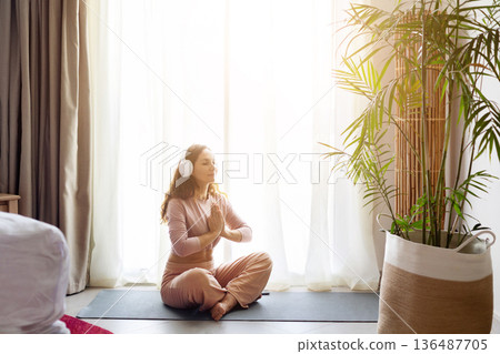 Adult caucasian woman meditating with headphones on yoga mat in hotel room Adult caucasian woman meditating with headphones on yoga mat in hotel room 136487705