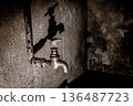 Close-up of an old rusty metal water tap mounted on a rough textured wall in a dark interior, abandoned room. 136487723