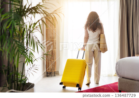 Rear view of woman standing near window with suitcase inside hotel room Rear view of woman standing near window with suitcase inside hotel room 136487729