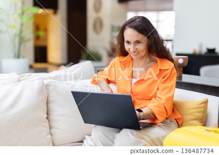 Adult woman using laptop on hotel sofa, remote work during travel stay Adult woman using laptop on hotel sofa, remote work during travel stay 136487734