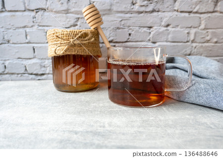 Honey jar with honeycomb, cap of tee and wood spoon stay on the table near napkin. 136488646