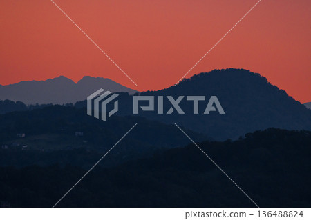 Mountain silhouettes at sunset with dramatic orange sky, serene landscape showcasing natural beauty. 136488824