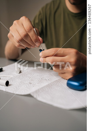 Close-up vertical cropped shot of man performing maintenance on electronic cigarette with cotton swab, ensuring optimal functioning and cleanliness for better vaping experience and improved hygiene. Close-up vertical cropped shot of man performing maintenance on electronic cigarette with cotton swab, ensuring optimal functioning and cleanliness for better vaping experience and improved hygiene. 136489267