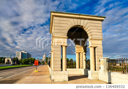John Ireland Blvd Bridge in St Paul, Minnesota features a historic stone gatehouse arch with the State Capitol dome in the background under a cloudy sky 136489332