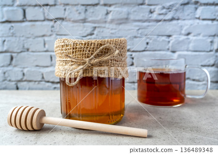 Honey glass jar with honeycomb, cup of tee and wood spoon stay on the stone table. 136489348