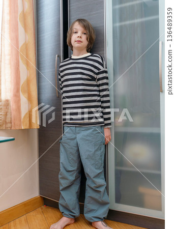 Vertical full body portrait of a barefoot boy standing by a wardrobe. Casual kid fashion Vertical full body portrait of a barefoot boy standing by a wardrobe. Casual kid fashion 136489359