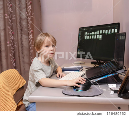 Young boy sitting at desk using computer mouse. Child learning online at home with laptop Young boy sitting at desk using computer mouse. Child learning online at home with laptop 136489362