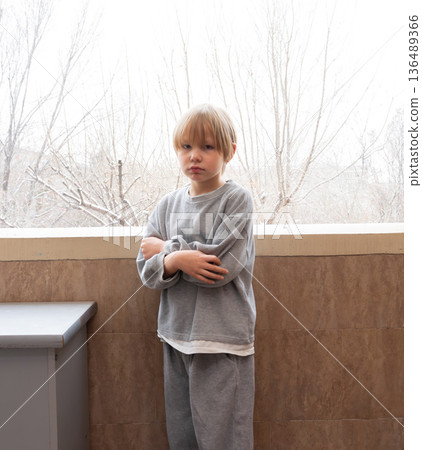 Serious young boy with arms crossed on a balcony. Portrait of an unhappy child in winter 136489366