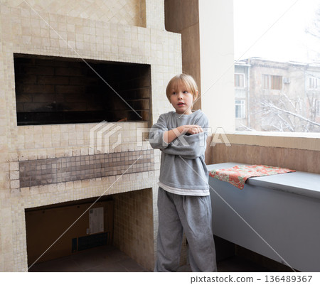 Young boy standing on a balcony next to a fireplace. Child feeling cold in winter 136489367