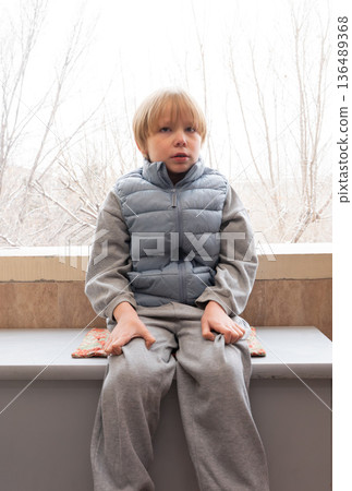 Sad young boy sitting alone near window. Unhappy child portrait indoors. Mental health concept Sad young boy sitting alone near window. Unhappy child portrait indoors. Mental health concept 136489368