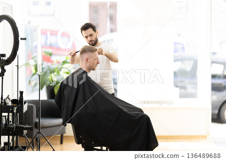 Barber giving modern haircut to male customer in barbershop Barber giving modern haircut to male customer in barbershop 136489688