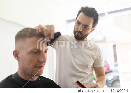 Professional barber cutting male client's hair in salon Professional barber cutting male client's hair in salon 136489694