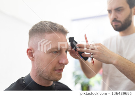 Barber giving client a modern haircut in salon Barber giving client a modern haircut in salon 136489695