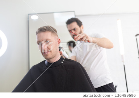 Professional barber cutting man's hair in modern barbershop 136489696