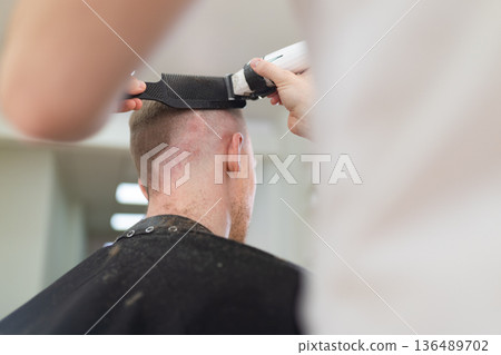 Barber cutting man's hair with electric clipper 136489702