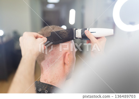 Hairdresser cutting client's hair with electric clipper 136489703