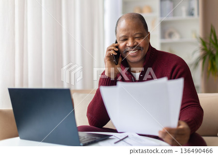 Mature black man talking on smartphone while checking documents at home Mature black man talking on smartphone while checking documents at home 136490466