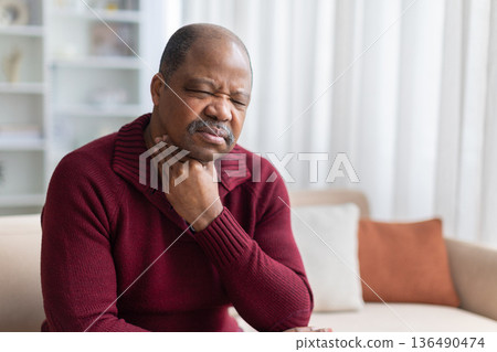 Mature black man touching throat, experiencing sore throat at home Mature black man touching throat, experiencing sore throat at home 136490474