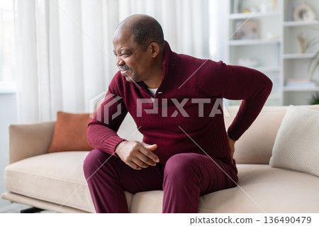 Mature black man holding lower back in pain while sitting on sofa 136490479