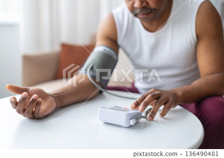 Mature black man measuring blood pressure at home using digital monitor Mature black man measuring blood pressure at home using digital monitor 136490481