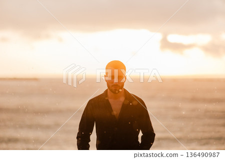 Young man standing by ocean at golden hour Young man standing by ocean at golden hour 136490987