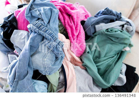 Colorful pile of mixed textiles on sofa showing laundry chaos 136491348
