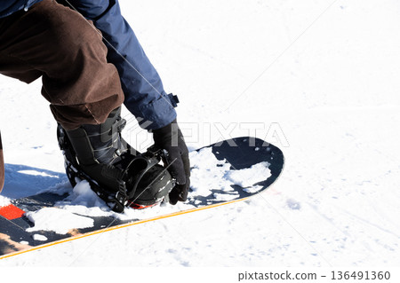 Snowboarder adjusting boot binding on snowy slope Snowboarder adjusting boot binding on snowy slope 136491360