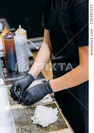 Chef in gloves spreads sushi rice on nori sheets for maki rolls in restaurant kitchen 136491833