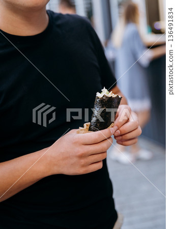 Close up of person holding sushi hand roll street food snack outdoors Close up of person holding sushi hand roll street food snack outdoors 136491834