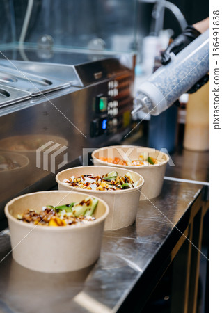 Sauce being poured over takeaway salad bowls on stainless counter in restaurant kitchen Sauce being poured over takeaway salad bowls on stainless counter in restaurant kitchen 136491838