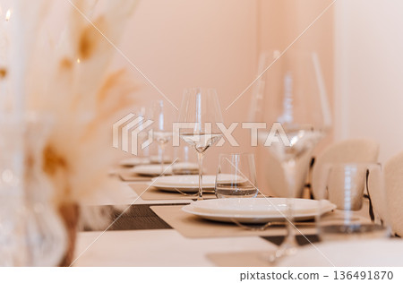 Wine glasses and place settings on elegant banquet table in soft neutral interior Wine glasses and place settings on elegant banquet table in soft neutral interior 136491870