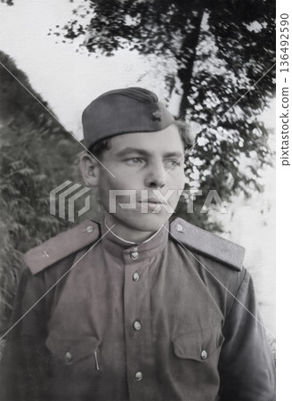 A vintage portrait of a young Soviet Army soldier wearing a cap. Retro photo from 1955. 136492590