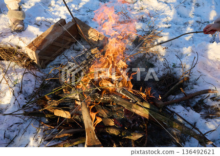 Inviting winter bonfire with crackling flames in snowy landscape and people around. 136492621