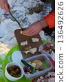Winter picnic with a person cooking bacon on a stick outdoors with snow and food. 136492626
