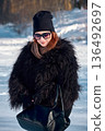 Chic Winter Outfit: Woman in Fur Coat, Black Hat, and Sunglasses on Snowy Day. 136492697