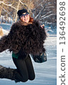A joyful woman in a stylish fur coat jumps for joy in a snowy winter landscape in a good mood. 136492698